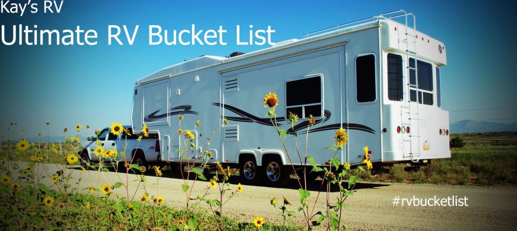 Pick up with hitched fifth wheel camper on dirt road with sunflowers and New Mexico blue sky above.